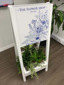 White folding pavement sign with built in storage for flowers or weights