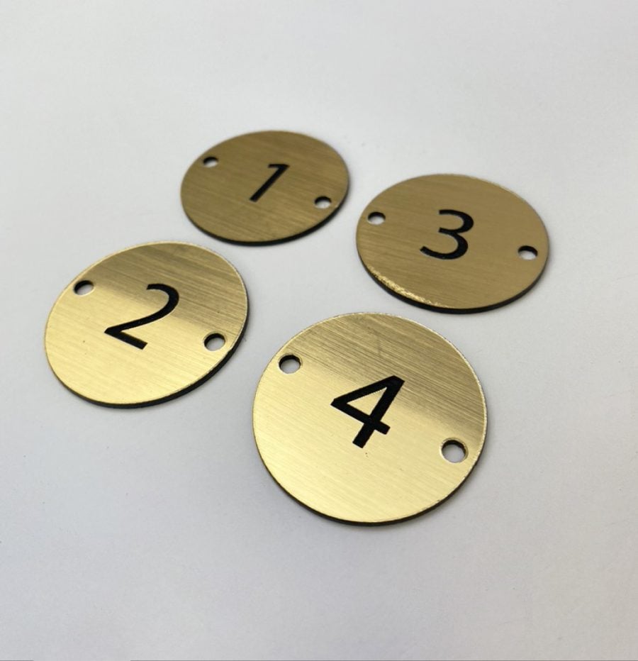 Small round gold coloured metal looking disc with a table numbers